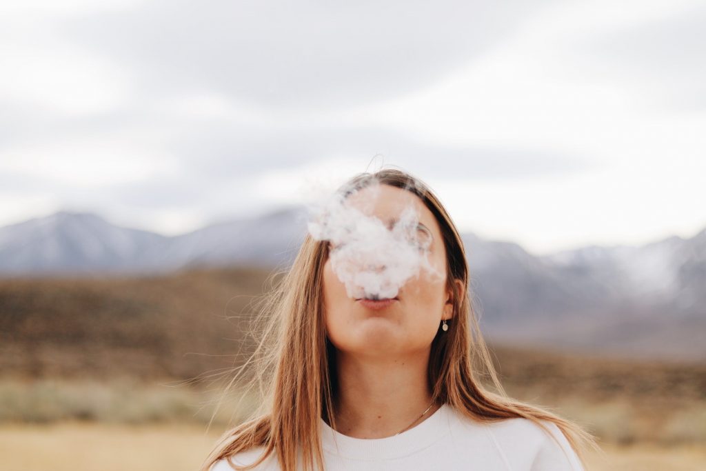A woman wearing a white crew neck shirt smoking in the open air