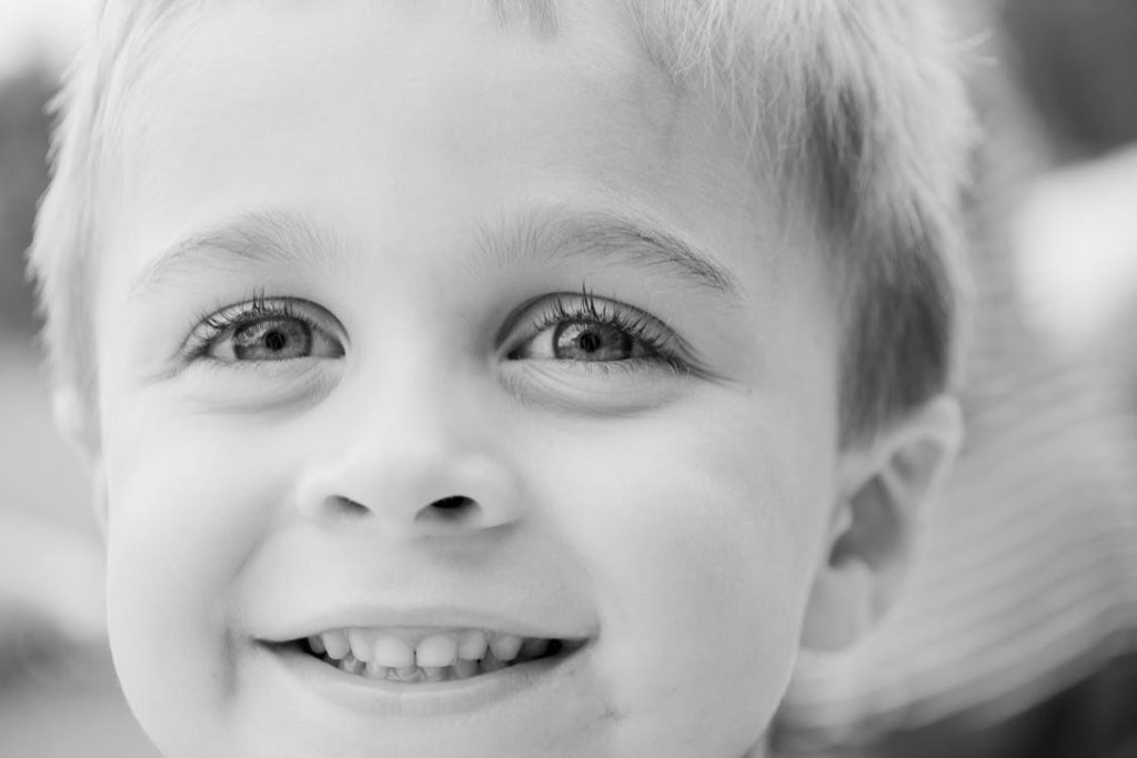 a grayscale picture of a toddler smiling with his eyes facing the camera