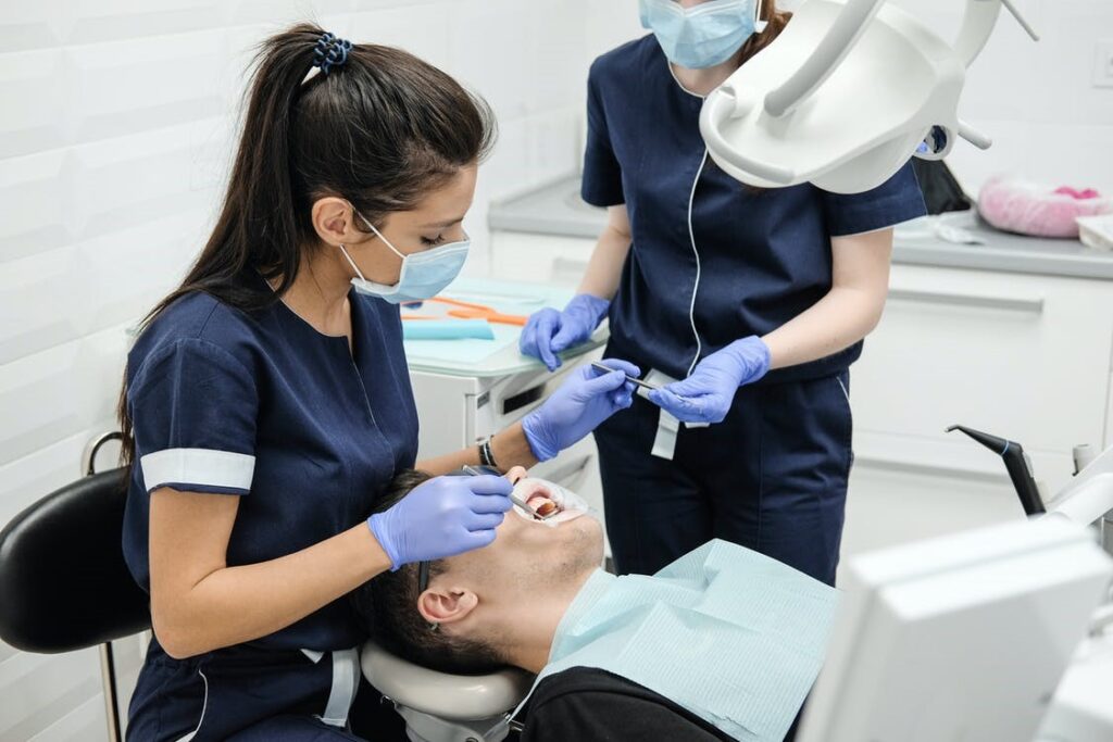 A dentist treating the teeth of a patient with surgical equipment and a nurse's help. 