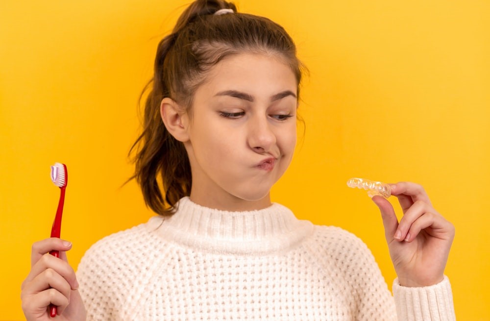 Girl holding a toothbrush and Invisalign