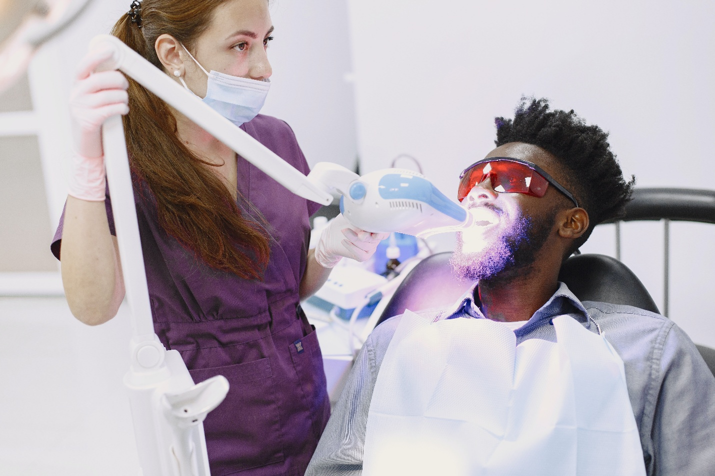 A dentist using a laser to whiten a man’s teeth.