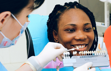 A dentist is matching dental veneers to a woman’s teeth.