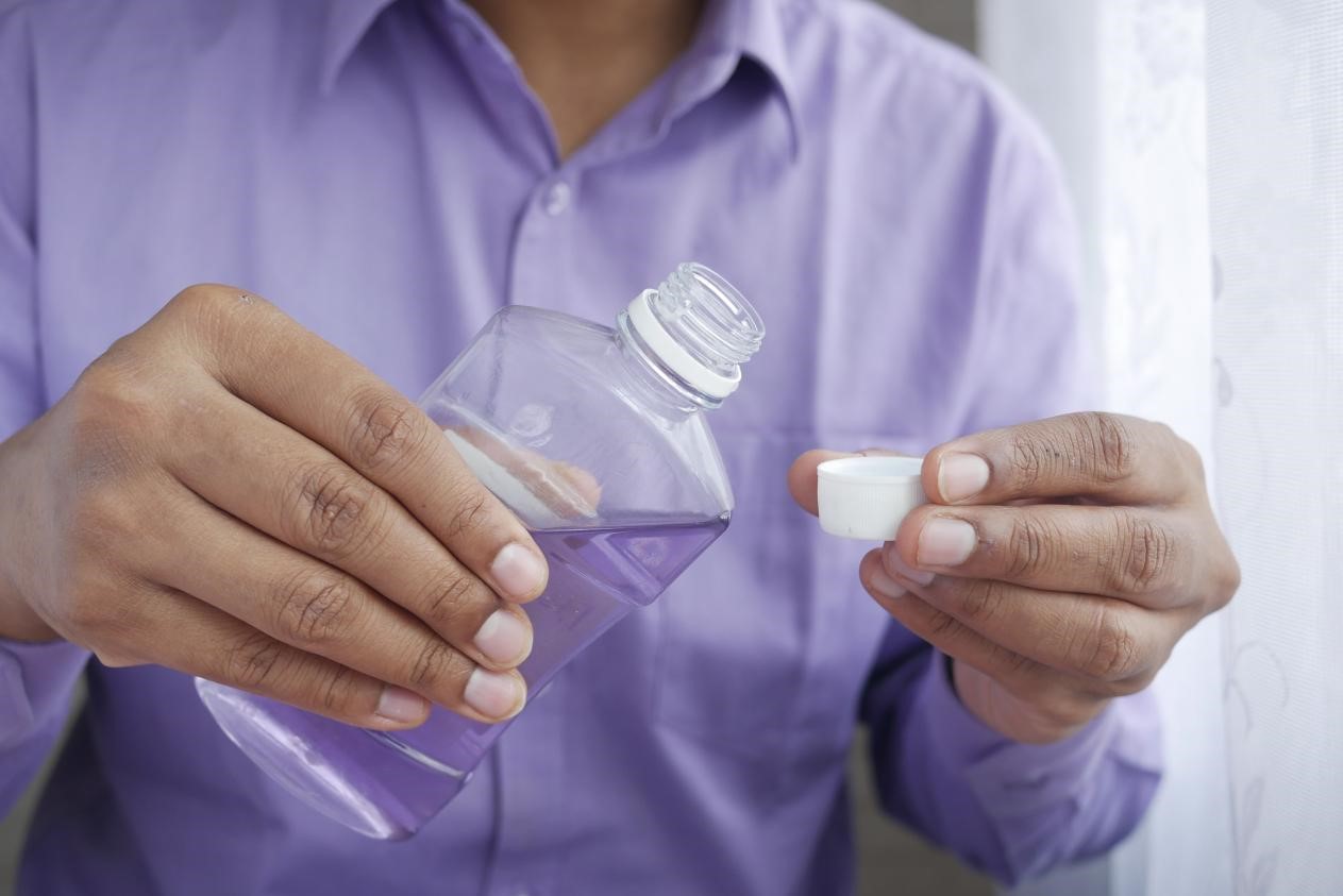 A man pouring mouthwash into a bottle cap