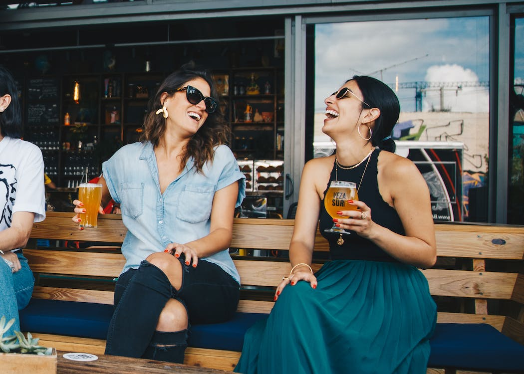 Two women sitting on a wooden bench, laughing confidently