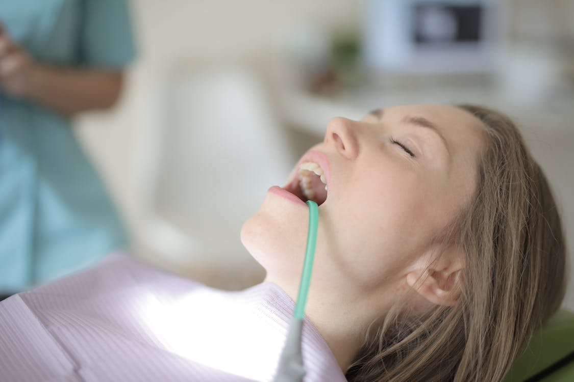 A closeup of a female patient with a suction tube in her mouth during a dental cleaning for bad breath treatment