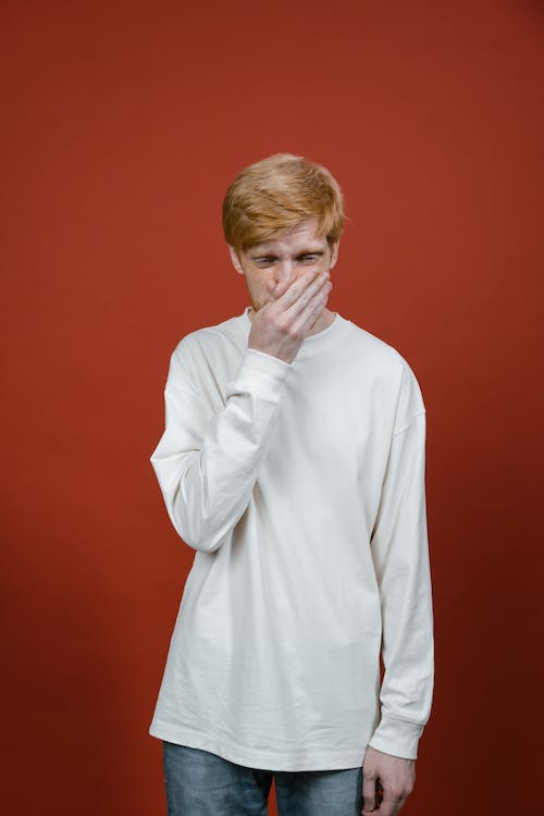 A man in a white sweater covering his mouth due to bad breath