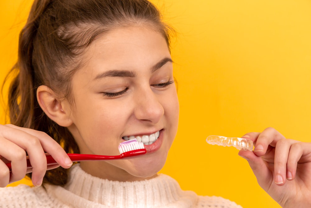 A girl is brushing her teeth and holding an Invisalign