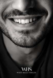 Black-and-white portrait of a man smiling naturally, highlighting his teeth and overall smile appearance.